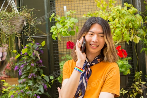 Vista previa: Joven gay asiático sonriente hablando por teléfono móvil al aire libre