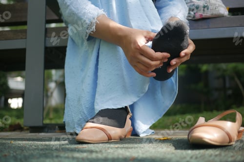 Preview: young women message her feet sitting on park bench