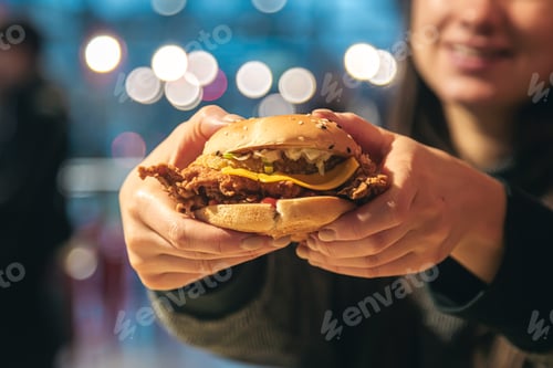 Preview: An appetizing chicken burger in female hands in a fast food restaurant, close up.