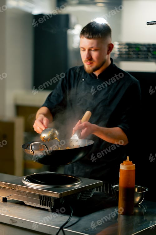 Preview: in professional kitchen the chef prepares wog noodles with vegetables on a large frying pan