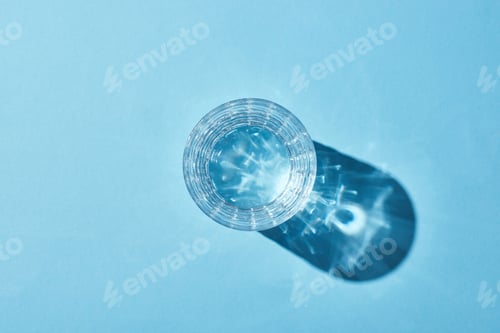 Preview: top view of glass with clear water on blue background with shadow