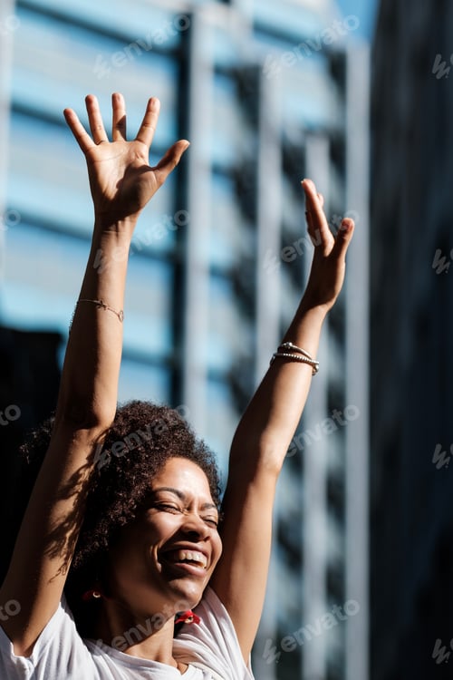 Preview: Successful curly woman celebrating in the street.