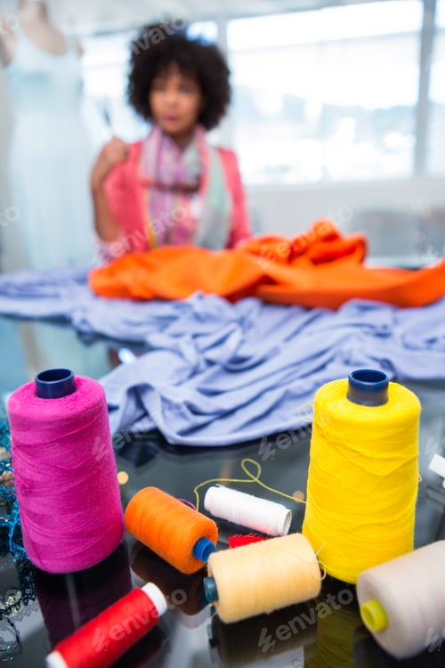 Preview: Close up of threads on table with female fashion designer in background