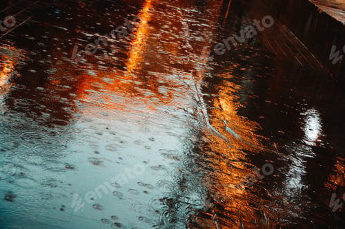 Preview: Abstract photography of rain. Raindrops on asphalt in the light of evening lights.