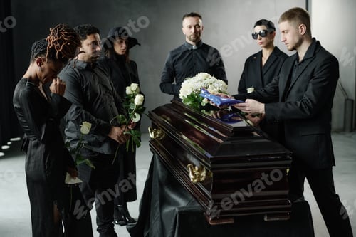 Preview: Young and Middle Aged Adults Honoring Deceased with Flowers Beside Wooden Casket
