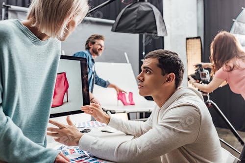 Preview: selective focus of handsome man gesturing near woman and computer monitor in photo studio