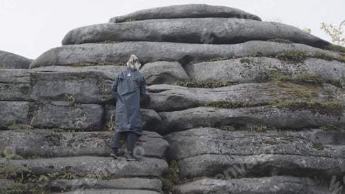 Preview: Rear view of a man in a long jacket and colored hair trying to climb a stony mountain. Stock footage