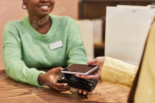 Preview: Close up of unrecognizable young woman paying via phone NFC technology in store