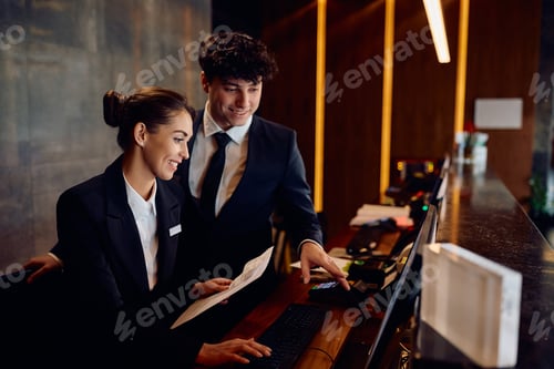 Preview: Happy receptionists cooperating while working on a computer at hotel front desk.