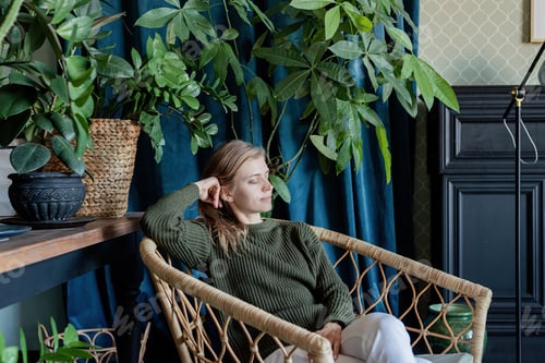 Preview: Young blonde woman sitting in comfortable chair surrounded with plants