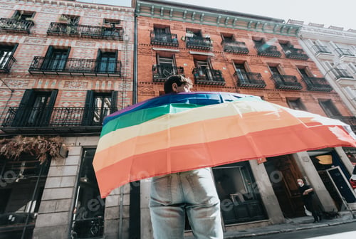 Preview: Young man holding a pride lgtbi rainbow flag on his back while walking on the streets