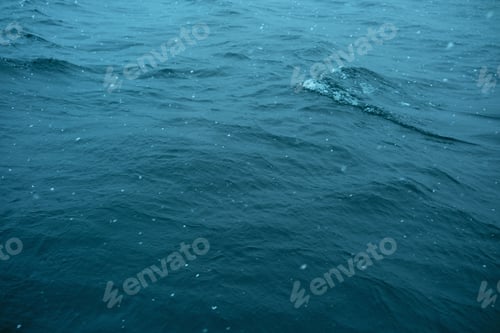Preview: Dark blue water surface with small waves and falling snow in cloudy weather.