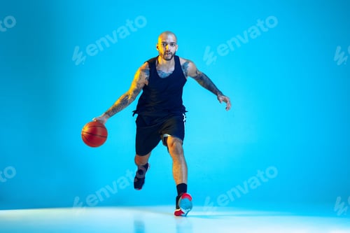 Preview: Young basketball player training isolated on blue studio background in neon light