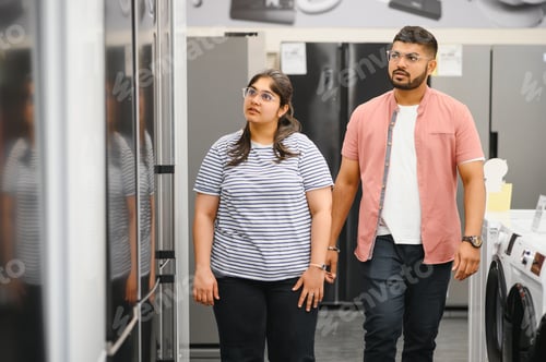 Preview: Young indian couple, satisfied customers choosing fridges in appliances store