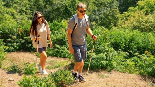 Preview: A man and a woman walk along a mountain trail with walking sticks. Trekking concept.