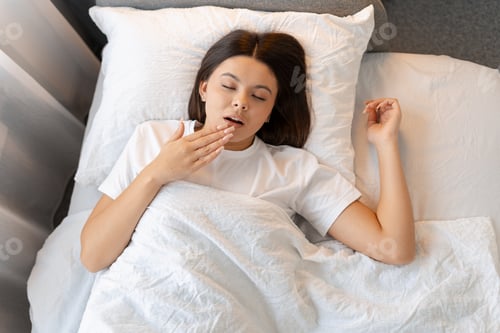 Preview: Young woman yawning and feeling tired in bed, waking up in the morning