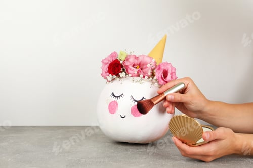 Preview: Female hands doing halloween makeup on pumpkin against white background