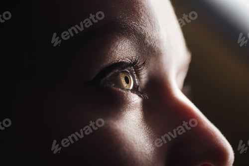 Preview: close up view of young woman eye with eyelashes and eyebrow looking away in dark