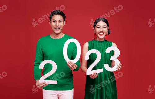 Preview: Happy asian couple in green casual attire showing number 2023 greeting happy new year