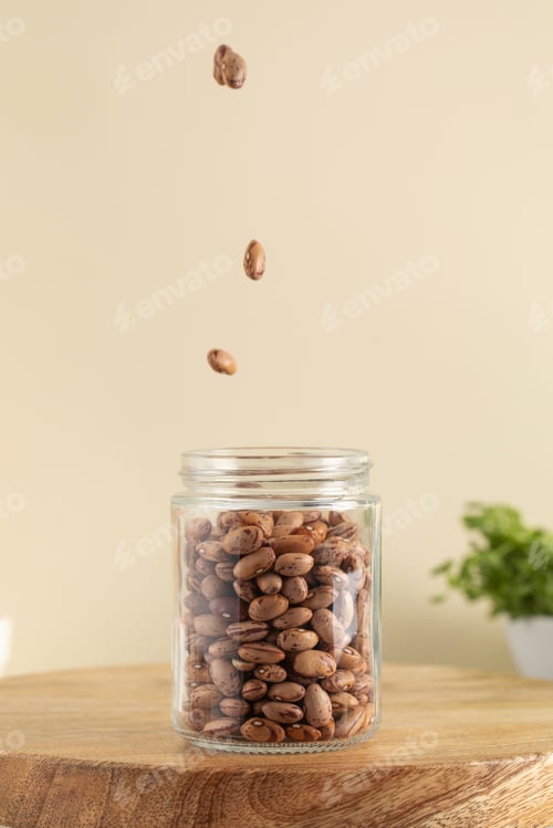 Preview: Raw pink beans fall into a glass jar on a beige background. Vegetable protein. Vegetarianism.