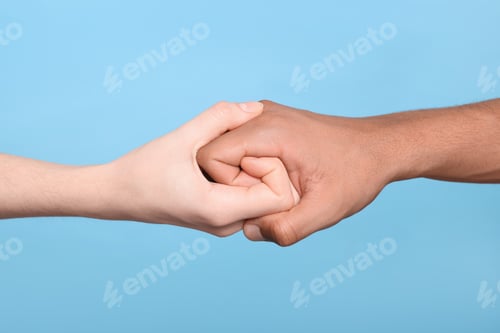 Preview: International relationships. People strongly joining hands on light blue background, closeup