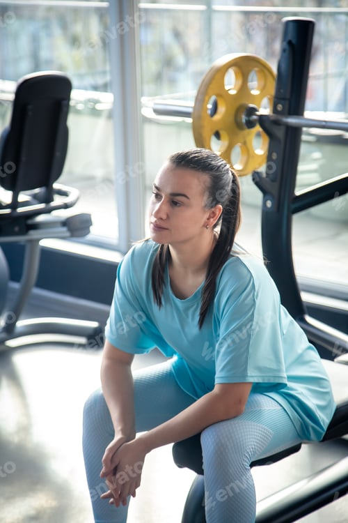 Preview: Tired young woman resting while sitting after working out in the gym.