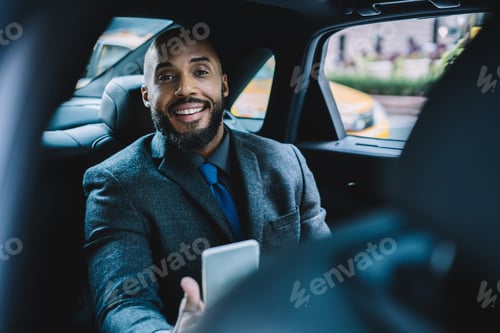 Preview: Cheerful African American businessman using smartphone in car