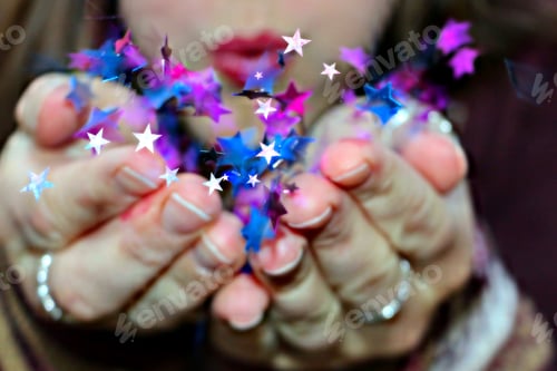 Preview: Closeup young woman blowing colorful star shaped confetti celebration