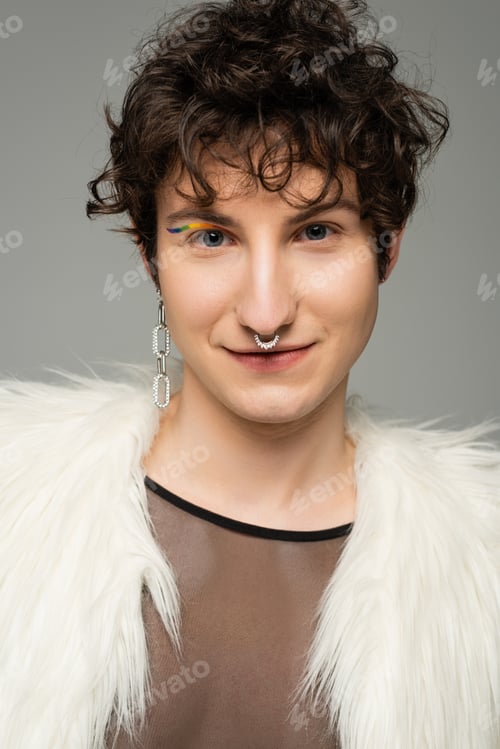 Preview: portrait of positive bigender person with silver nose piercing and rainbow eye liner looking at