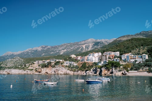 Preview: Fishing boats are moored in the sea near colorful hotels on a rocky slope. Przno, Montenegro