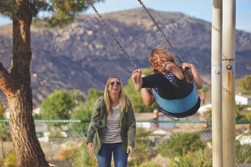 Preview: Mom and daughter laughing and having fun at the park on a swing mother
