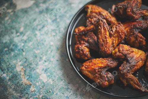 Preview: Grilled chicken wings on a black ceramic plate. Placed on a stone