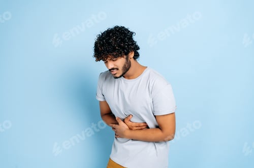 Preview: Stomach ache. Indian guy hunching and holding his belly, suffers from pain in the abdomen or stomach