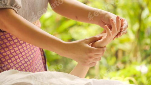 Preview: Massage therapist massaging woman's hand at spa.