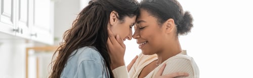 Preview: curly multiracial woman hugging cheerful girlfriend with closed eyes at home, banner