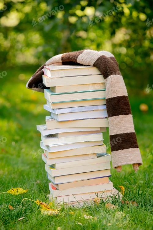 Preview: stack of books and a scarf on the green grass in autumn