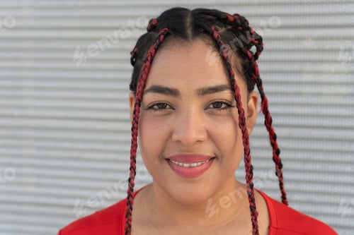 Preview: Young woman smiling with red and black braids posing in front of metal wall