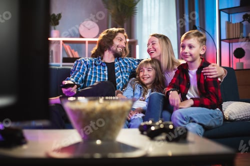 Preview: Young parents with kids relaxing on couch and watching TV