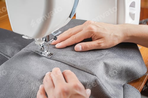Preview: Tailor Hands Stitching Gray Fabric On Modern Sewing Machine At Workplace In Atelier