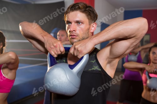 Preview: Young man lifting kettle against athletes
