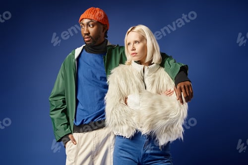 Preview: african american man hugging young woman in winter attire, diverse models standing on blue backdrop