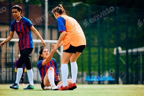 Preview: Soccer player assisting her teammate in getting up after a foul on playing field.