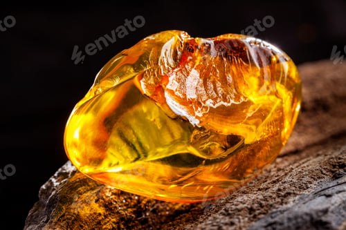 Preview: Natural amber. A piece of yellow transparent natural amber on large piece of dark stoned wood