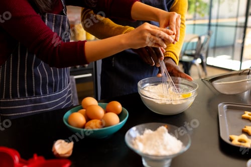 Preview: Midsection of diverse couple mixing dough for christmas cookies in kitchen