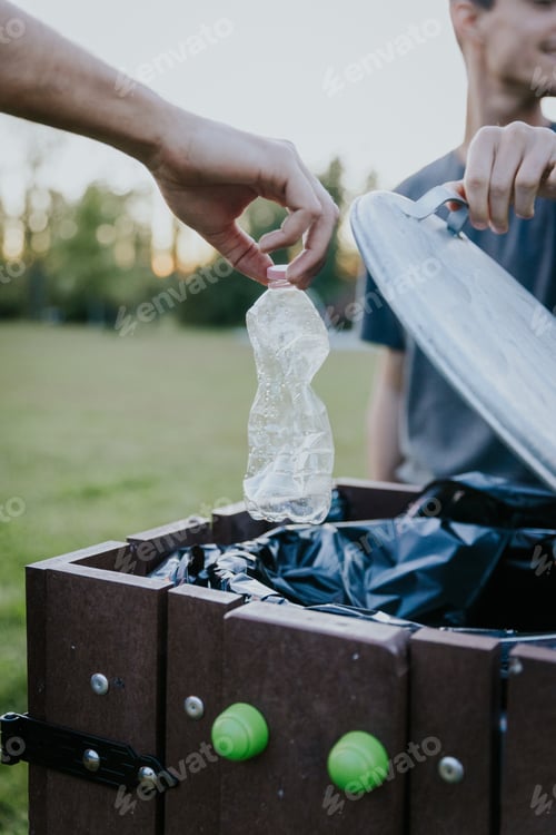 Preview: Volunteer throwing plastic bottle into trash bin in green park during autumn