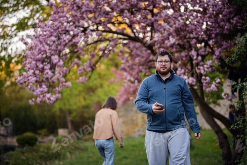 Preview: Man Walking with Phone Under Cherry Blossom Trees