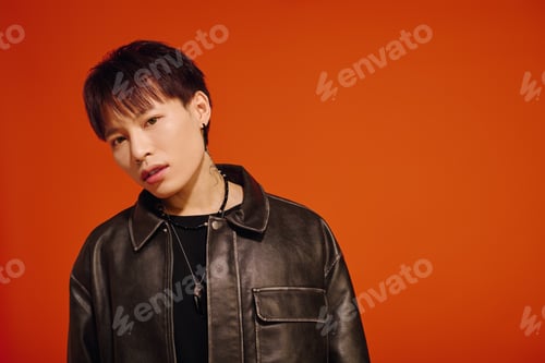 Preview: Stylish young Asian man poses confidently against a vibrant orange background in casual wear