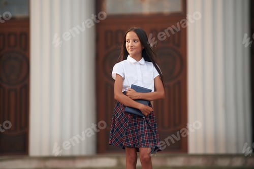 Visualização: Concepção de conhecimento. Menina da escola em uniforme está ao ar livre perto do prédio