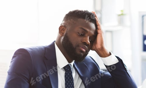 Preview: Exhausted young businessman working with laptop in office