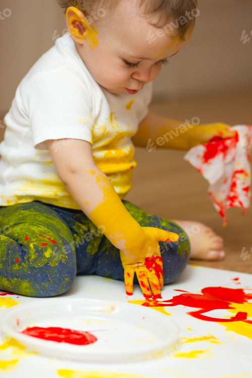 Preview: A funny baby, all stained in paint, draws on a large sheet of paper with red paint.